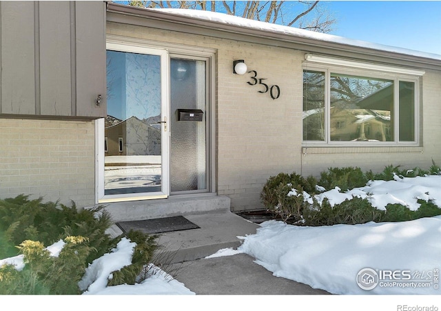 snow covered property entrance with brick siding