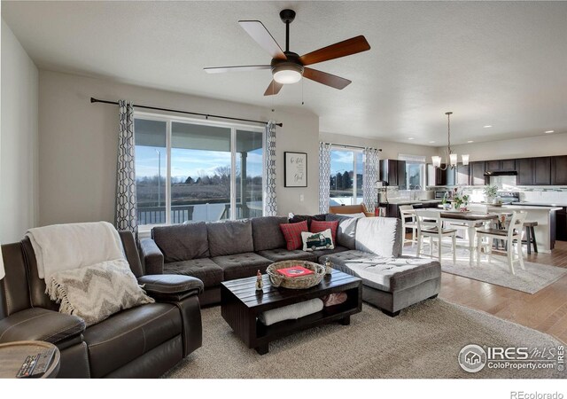 living room with ceiling fan with notable chandelier, a water view, and light wood-style floors