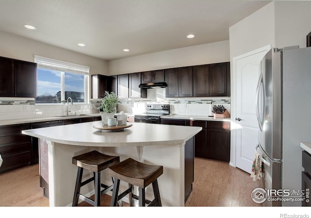 kitchen featuring a breakfast bar, stainless steel appliances, a sink, a kitchen island, and under cabinet range hood