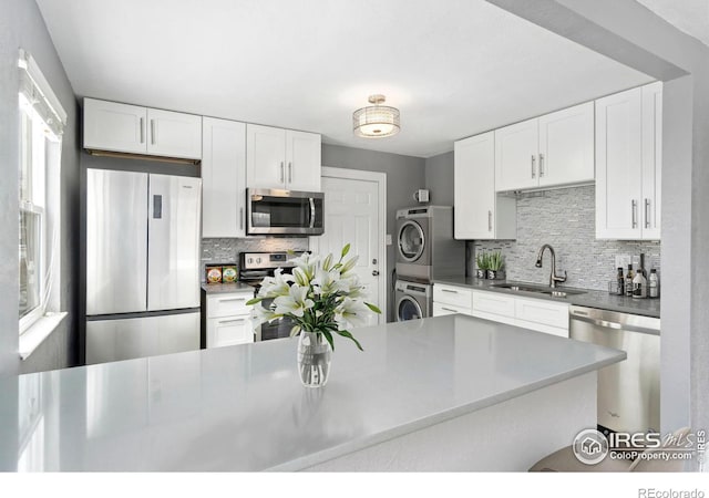 kitchen featuring a sink, white cabinetry, stacked washing maching and dryer, stainless steel appliances, and decorative backsplash