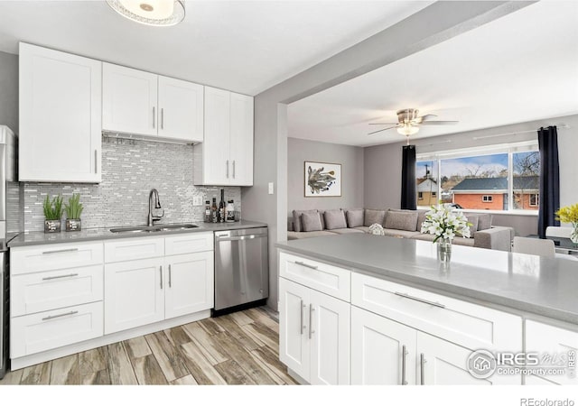 kitchen with light wood finished floors, open floor plan, dishwasher, light countertops, and a sink