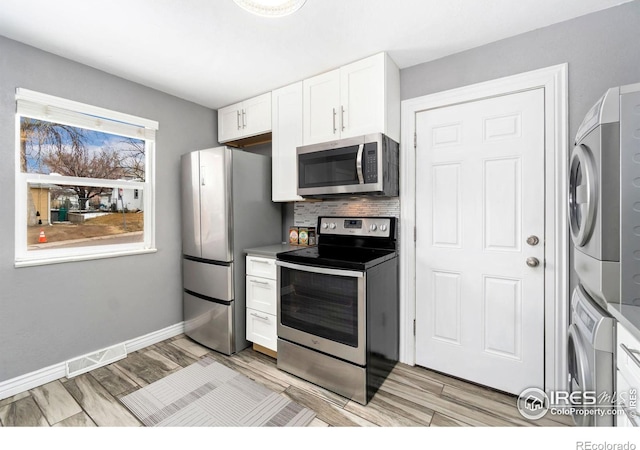 kitchen with visible vents, stacked washer and clothes dryer, stainless steel appliances, white cabinets, and baseboards