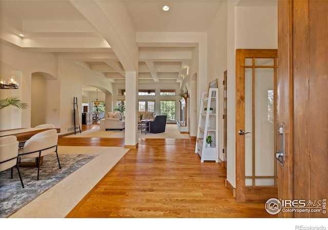 foyer entrance with coffered ceiling, beam ceiling, recessed lighting, arched walkways, and light wood-type flooring