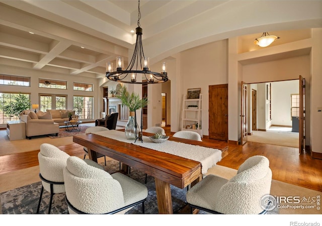 dining room featuring coffered ceiling, wood finished floors, arched walkways, an inviting chandelier, and a towering ceiling