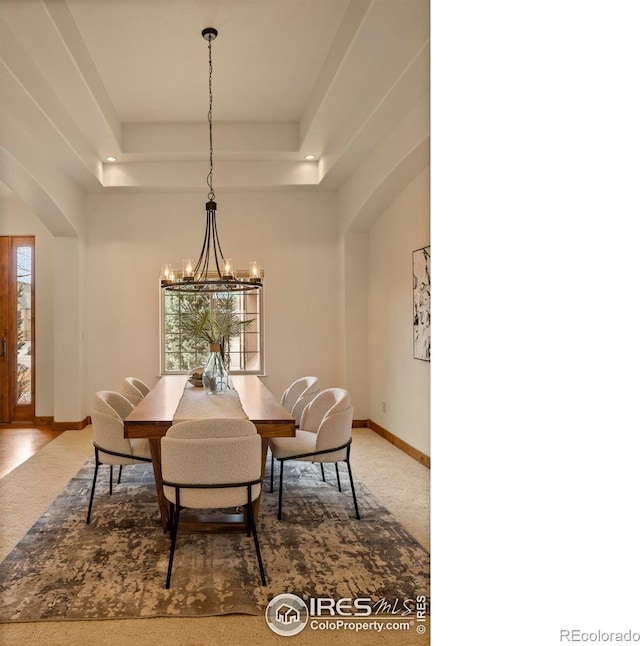 dining space featuring a tray ceiling, baseboards, arched walkways, and a chandelier