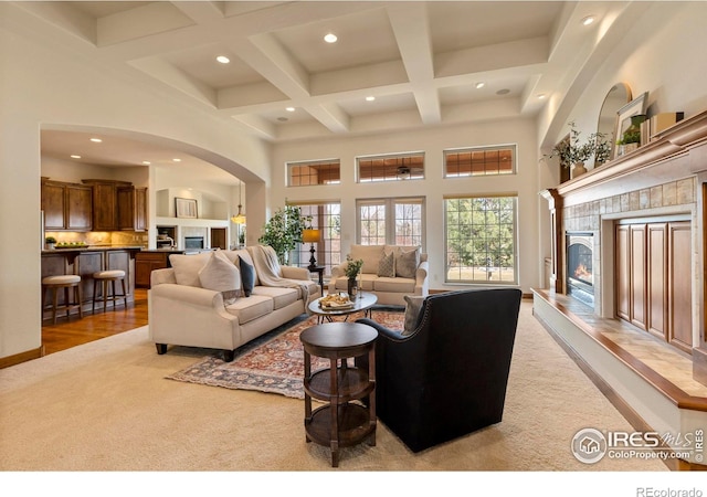 living area featuring a tiled fireplace, beam ceiling, recessed lighting, a towering ceiling, and coffered ceiling