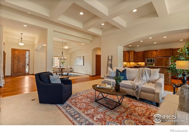 living area featuring arched walkways, beamed ceiling, coffered ceiling, and a high ceiling