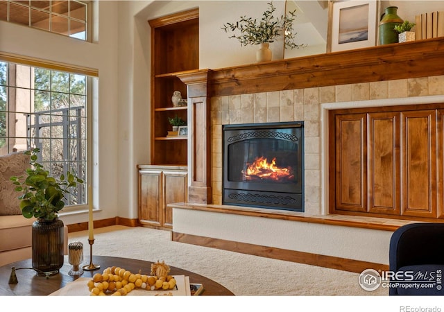 living room with built in shelves, baseboards, carpet floors, and a tile fireplace