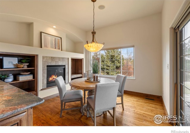 dining room with baseboards, light wood-style floors, and a tiled fireplace