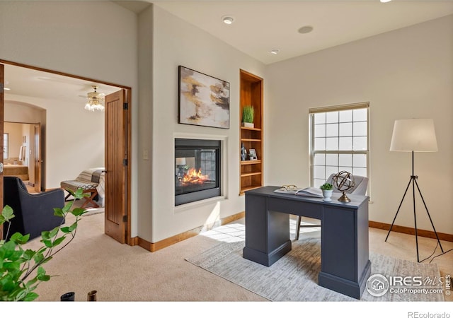 office featuring light carpet, built in shelves, baseboards, arched walkways, and a multi sided fireplace