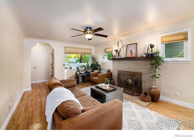 living area featuring arched walkways, a fireplace, baseboards, and wood finished floors