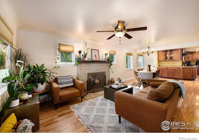 living area with ceiling fan with notable chandelier, a fireplace, light wood-type flooring, and baseboards