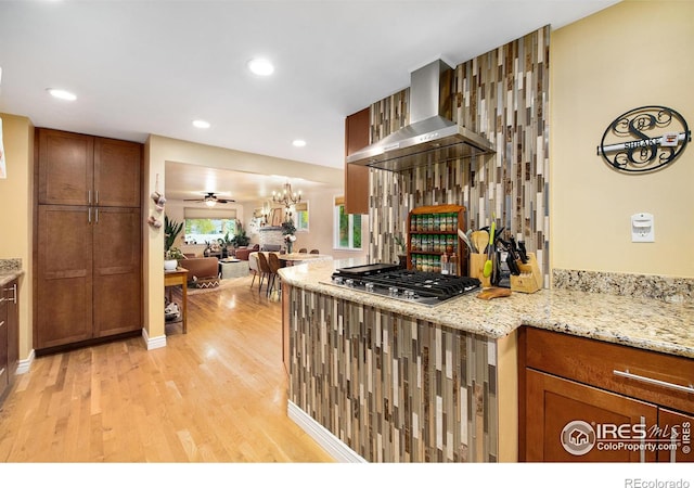 kitchen with light stone counters, open floor plan, light wood-style floors, stainless steel gas stovetop, and wall chimney range hood