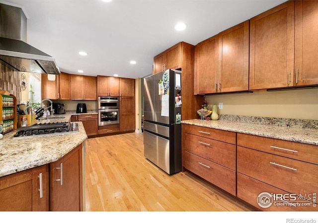 kitchen featuring recessed lighting, light wood-style flooring, brown cabinetry, stainless steel appliances, and wall chimney exhaust hood