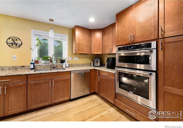 kitchen featuring brown cabinets, appliances with stainless steel finishes, light wood-style flooring, and a sink