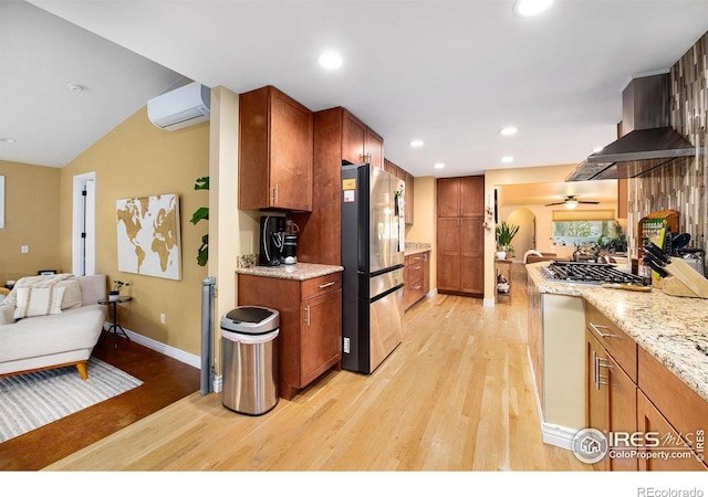 kitchen with stainless steel appliances, light stone countertops, an AC wall unit, and light wood finished floors