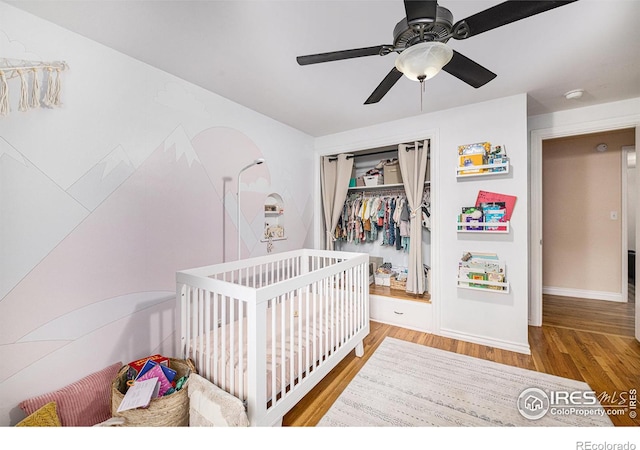 bedroom featuring a crib, baseboards, ceiling fan, wood finished floors, and a closet