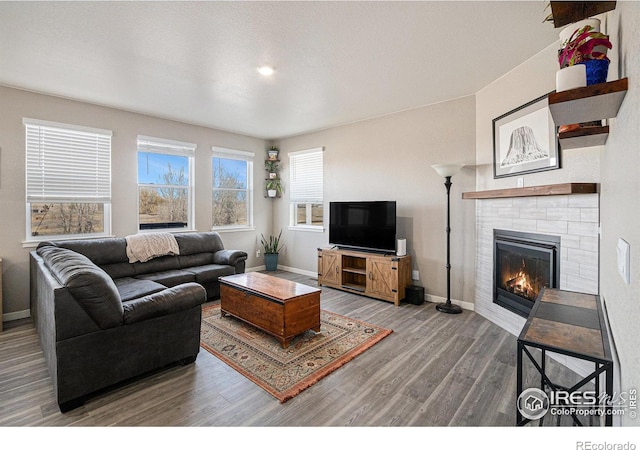 living room featuring a glass covered fireplace, baseboards, and wood finished floors