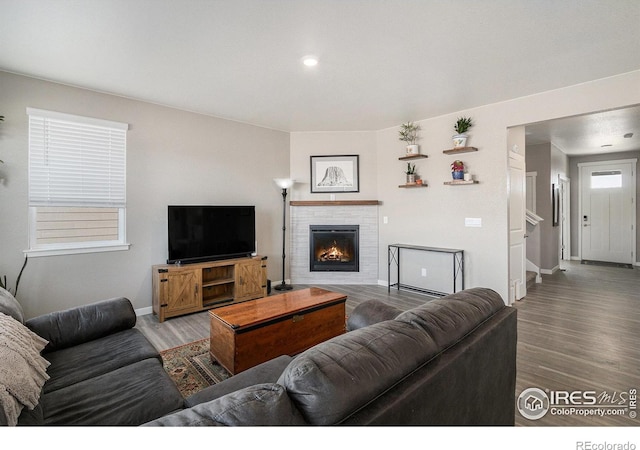 living room featuring stairway, wood finished floors, baseboards, and a lit fireplace