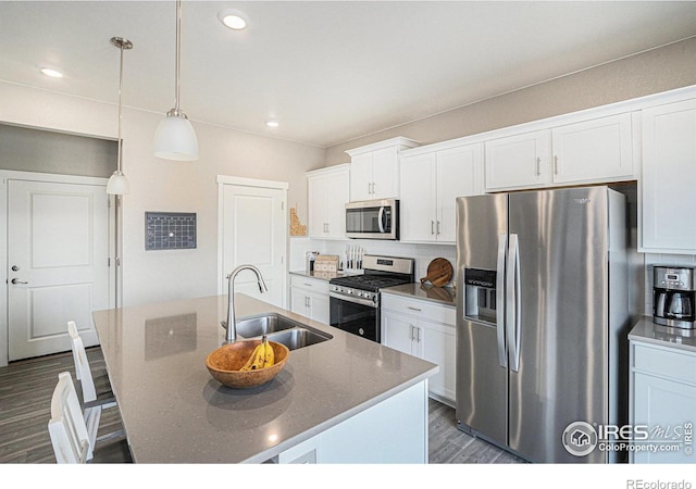 kitchen featuring dark wood finished floors, an island with sink, a sink, appliances with stainless steel finishes, and white cabinetry