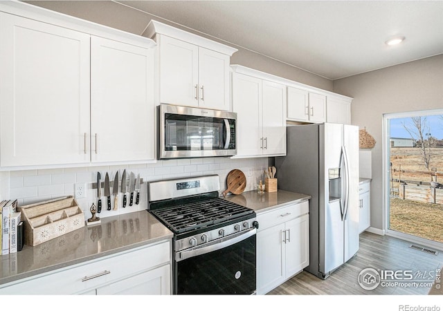 kitchen with visible vents, light wood-style flooring, appliances with stainless steel finishes, white cabinetry, and backsplash