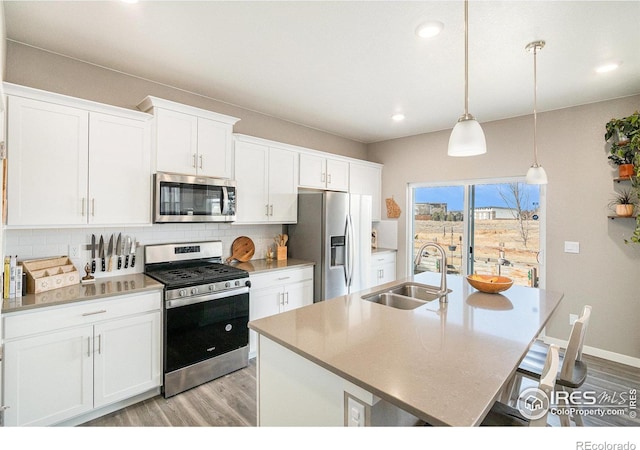 kitchen featuring light wood finished floors, a breakfast bar, a sink, stainless steel appliances, and tasteful backsplash