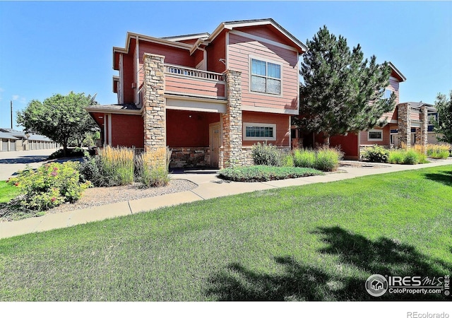 view of front of home featuring a front lawn, a balcony, and stone siding