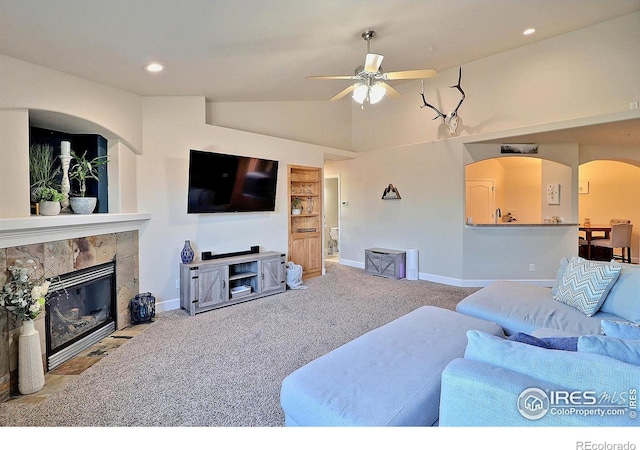 carpeted living room featuring ceiling fan, baseboards, lofted ceiling, a tile fireplace, and arched walkways