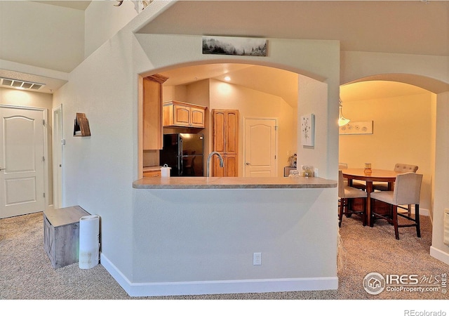 kitchen featuring visible vents, arched walkways, freestanding refrigerator, a sink, and light carpet