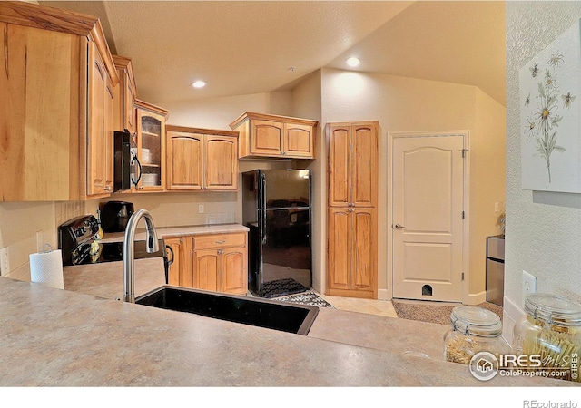 kitchen featuring lofted ceiling, a sink, black appliances, light countertops, and glass insert cabinets