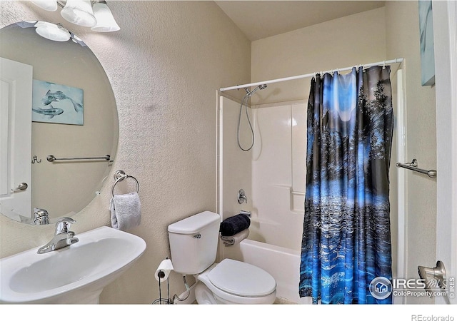 bathroom featuring a sink, toilet, shower / tub combo, and a textured wall