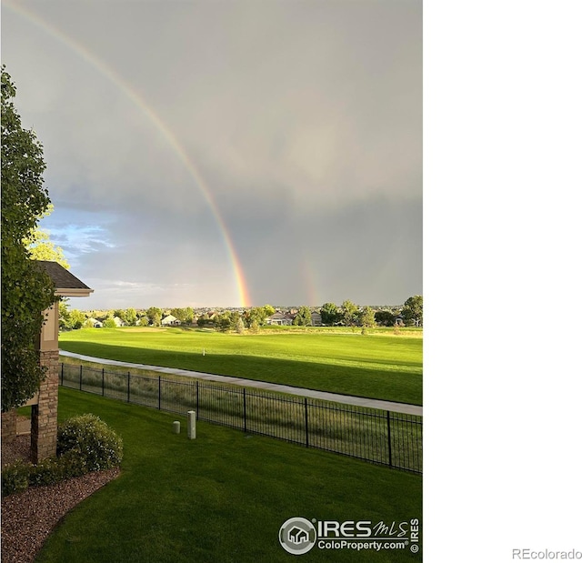 view of property's community featuring view of golf course, a yard, and fence