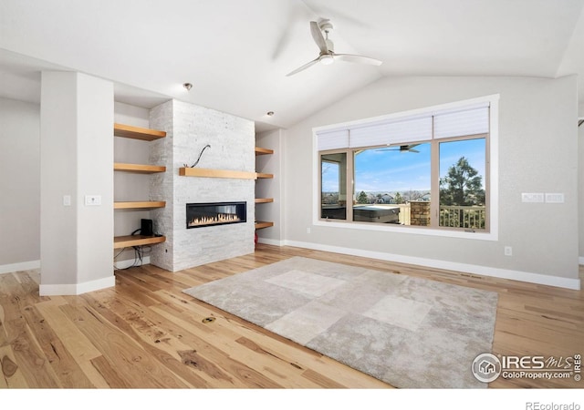 unfurnished living room featuring built in shelves, a ceiling fan, wood finished floors, a stone fireplace, and vaulted ceiling