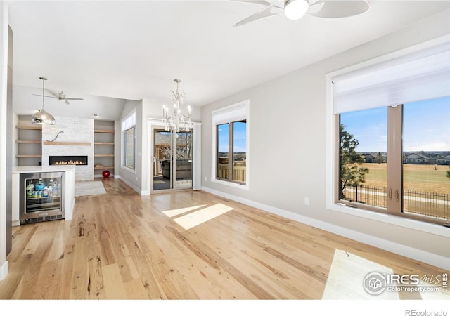 unfurnished living room with ceiling fan with notable chandelier, built in features, light wood-style floors, and a large fireplace