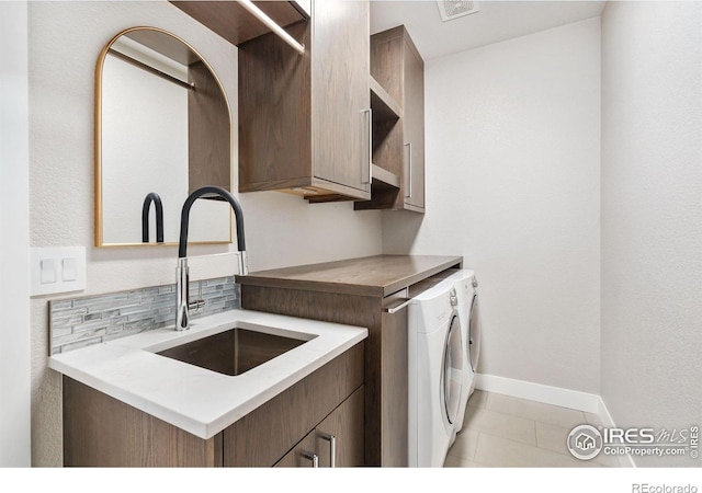 clothes washing area with visible vents, baseboards, washing machine and dryer, cabinet space, and a sink