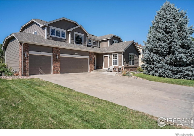 view of front of property featuring a front lawn, brick siding, driveway, and roof with shingles