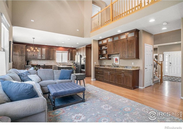 living room featuring stairway, recessed lighting, a towering ceiling, a notable chandelier, and light wood-type flooring