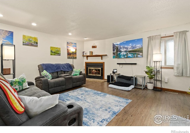 living room with a textured ceiling, a glass covered fireplace, wood finished floors, recessed lighting, and baseboards