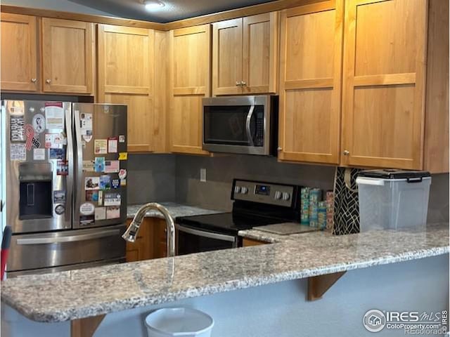 kitchen featuring a breakfast bar, a peninsula, stainless steel appliances, and light stone counters