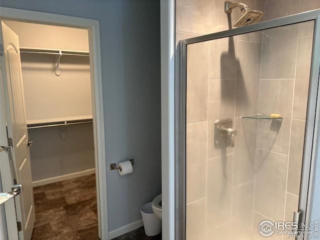 full bathroom featuring a shower stall, toilet, a walk in closet, and baseboards