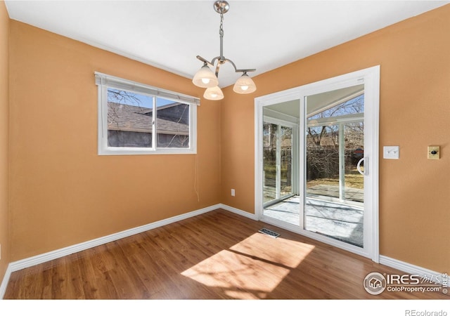 unfurnished dining area with a notable chandelier, wood finished floors, visible vents, and baseboards