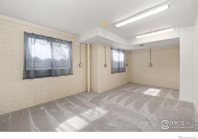 carpeted empty room featuring brick wall