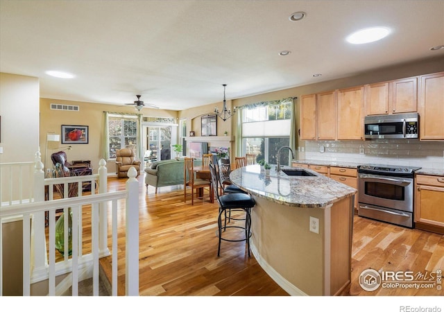 kitchen featuring light wood-type flooring, a sink, light stone counters, tasteful backsplash, and appliances with stainless steel finishes