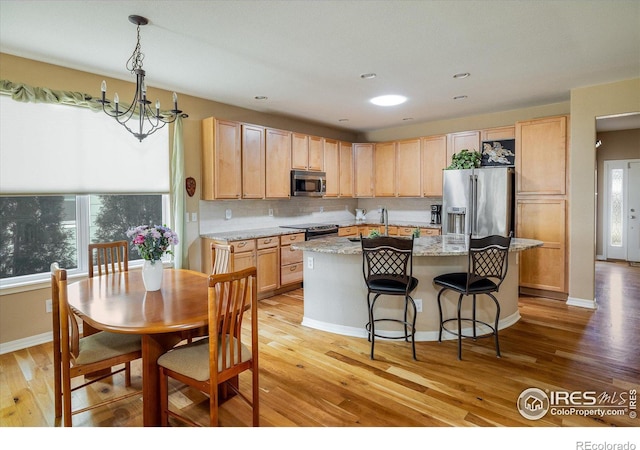 kitchen with light wood-style flooring, appliances with stainless steel finishes, a kitchen island with sink, and light brown cabinets