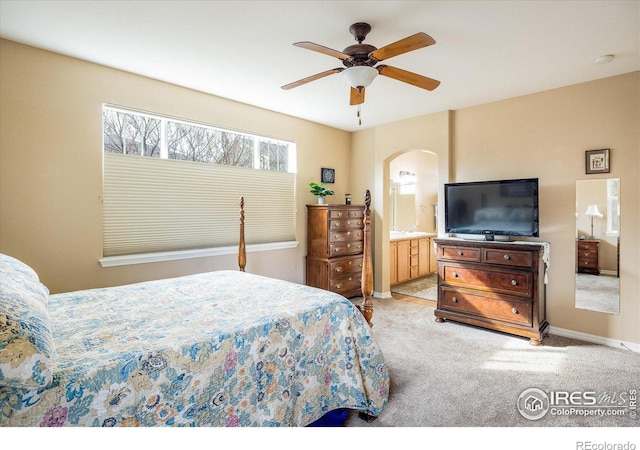 bedroom featuring ensuite bath, light colored carpet, baseboards, and ceiling fan