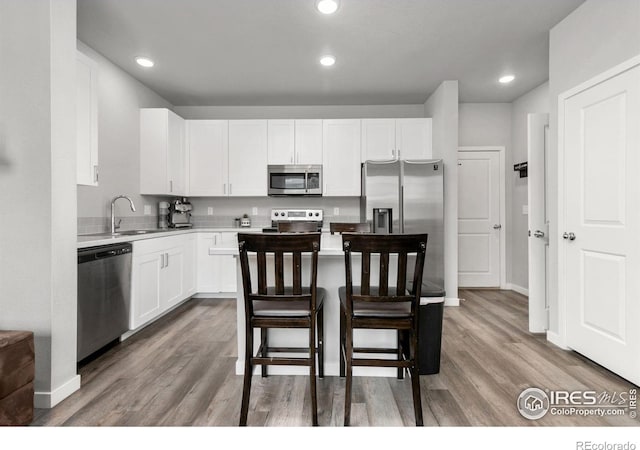 kitchen featuring appliances with stainless steel finishes, white cabinetry, a kitchen breakfast bar, and wood finished floors