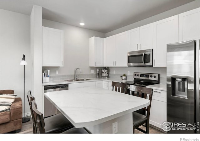 kitchen featuring a sink, stainless steel appliances, a kitchen bar, and white cabinetry