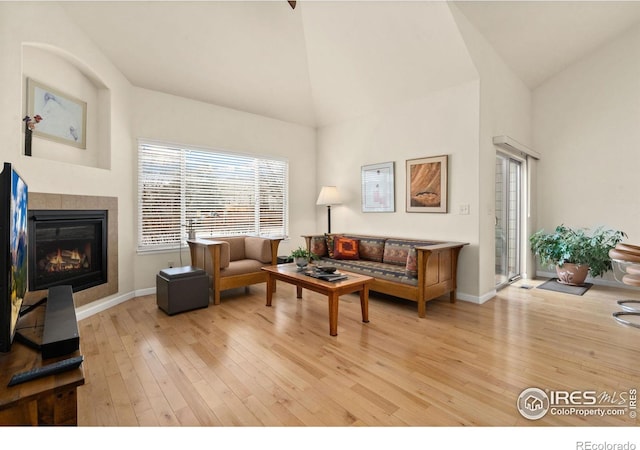 living area with a fireplace, baseboards, light wood finished floors, and high vaulted ceiling