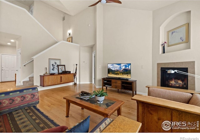 living room featuring a glass covered fireplace, a high ceiling, stairs, and wood finished floors