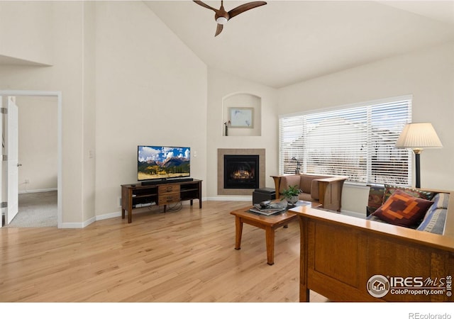 living area featuring ceiling fan, baseboards, light wood-type flooring, a fireplace, and high vaulted ceiling